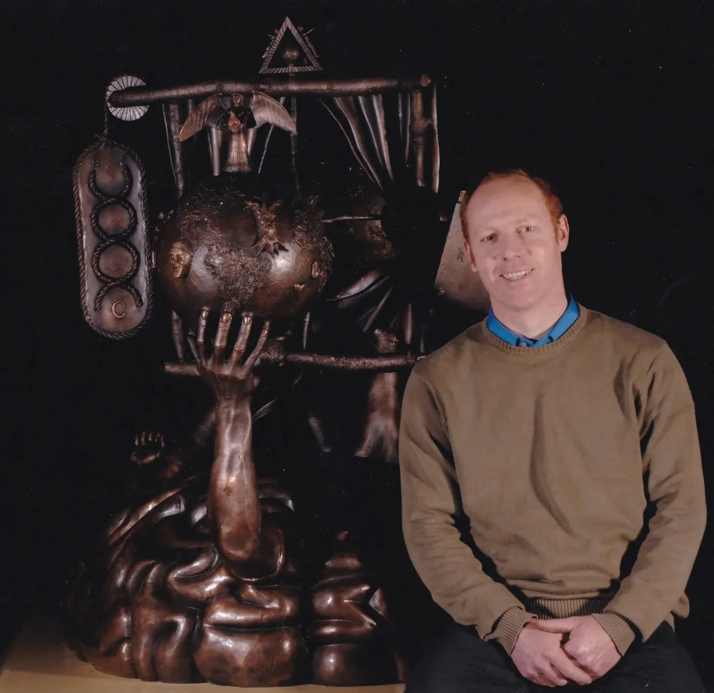 man sitting next to sculpture